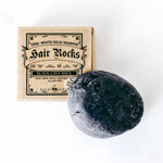 ScentCerae Hair Rocks natural shampoo bar with herbal ingredients, shown in a clear container with a textured surface.