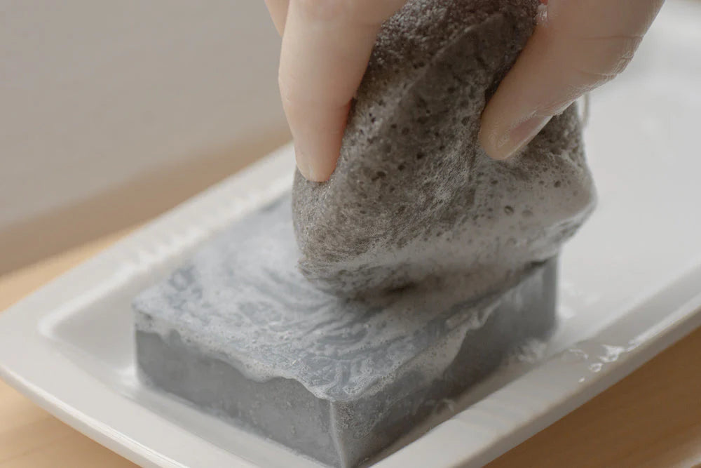 LUNA charcoal facial sponge by No Tox Life with soap bar, showing textured black sponge for gentle facial cleansing.
