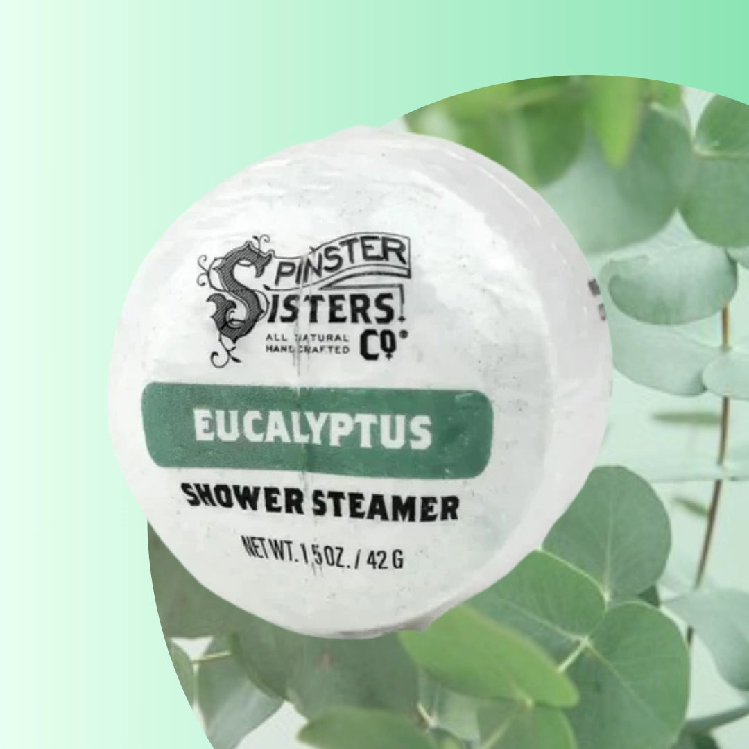 Eucalyptus shower steamers by Spinster Sisters, shown in a clear container with fresh green eucalyptus leaves.