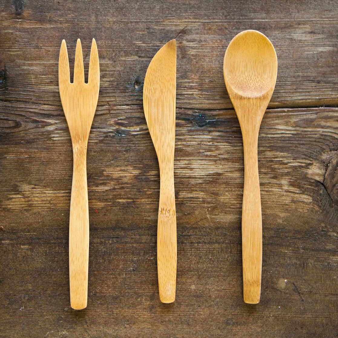 Set of bamboo utensils including fork, spoon, and knife from To-Go Ware on a wooden surface. Eco-friendly single utensils.